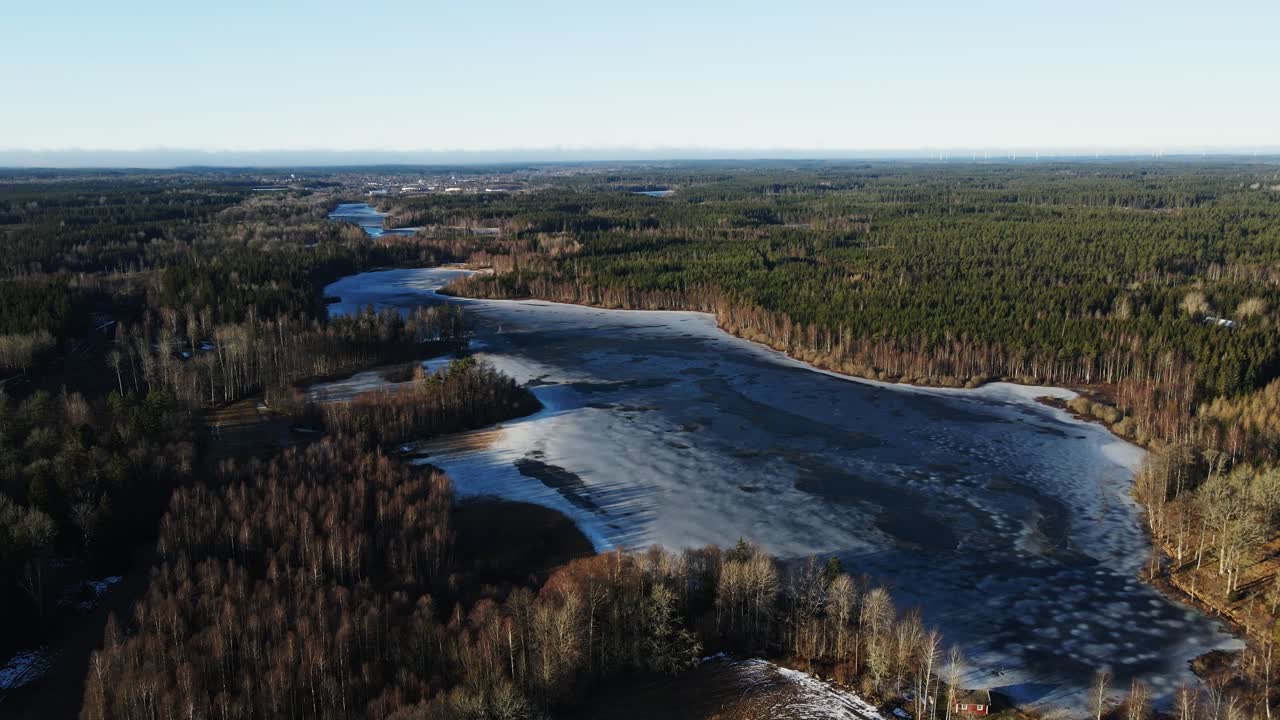 Beautiful aerial overview of a tranquil nature reservation with a frozen lake and a vast forest in rural Sweden on a sunny winter day