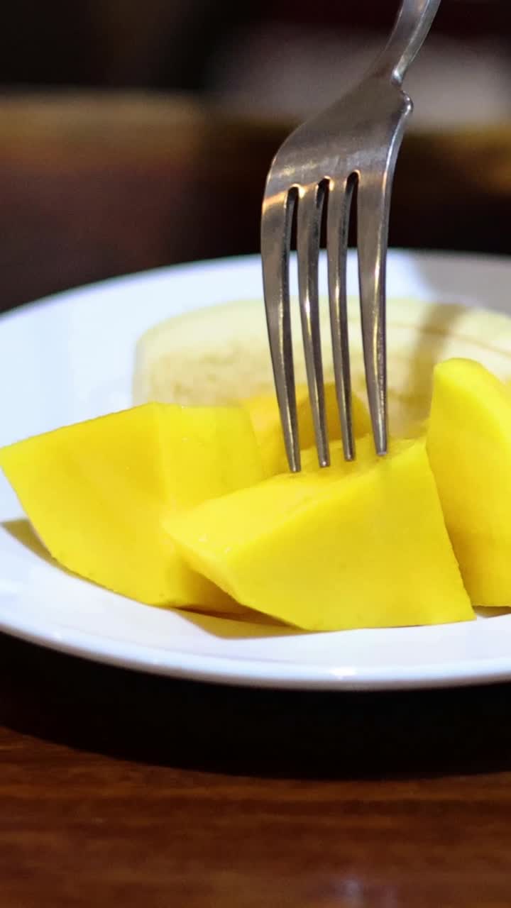 una persona corta y come mango con un tenedor.