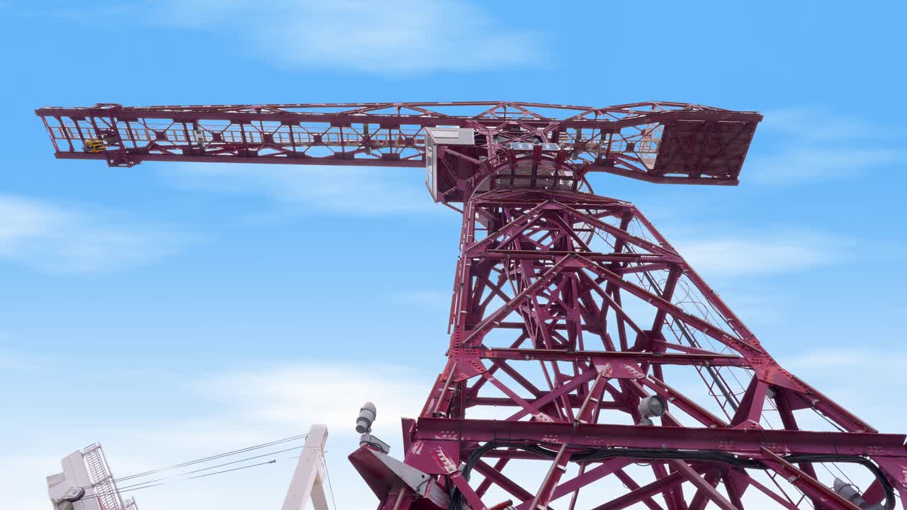A low-angle shot of a large, red, industrial crane against a blue sky with some scattered clouds