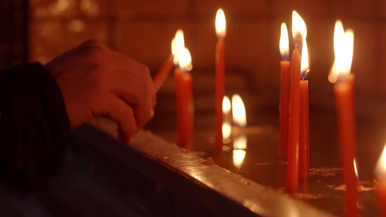 Mano che accende candele votive in una chiesa buia