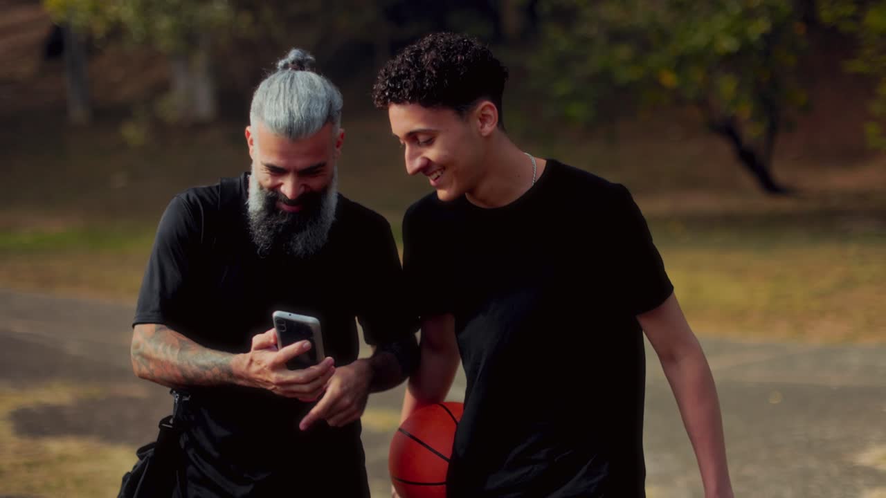 Two Men Share a Phone Screen and Conversation After a Basketball Session Outdoors
