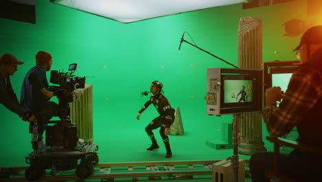 in the big film studio professional crew shooting blockbuster movie. director commands camera operator to start shooting green screen cgi scene with actor wearing motion tracking suit and head rig