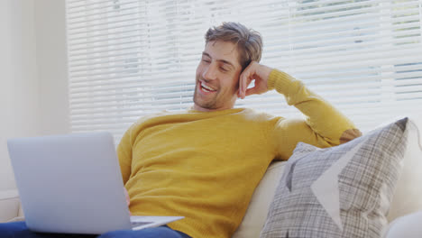 joven sonriente sentado en el sofá usando su computadora portátil 4k 4k