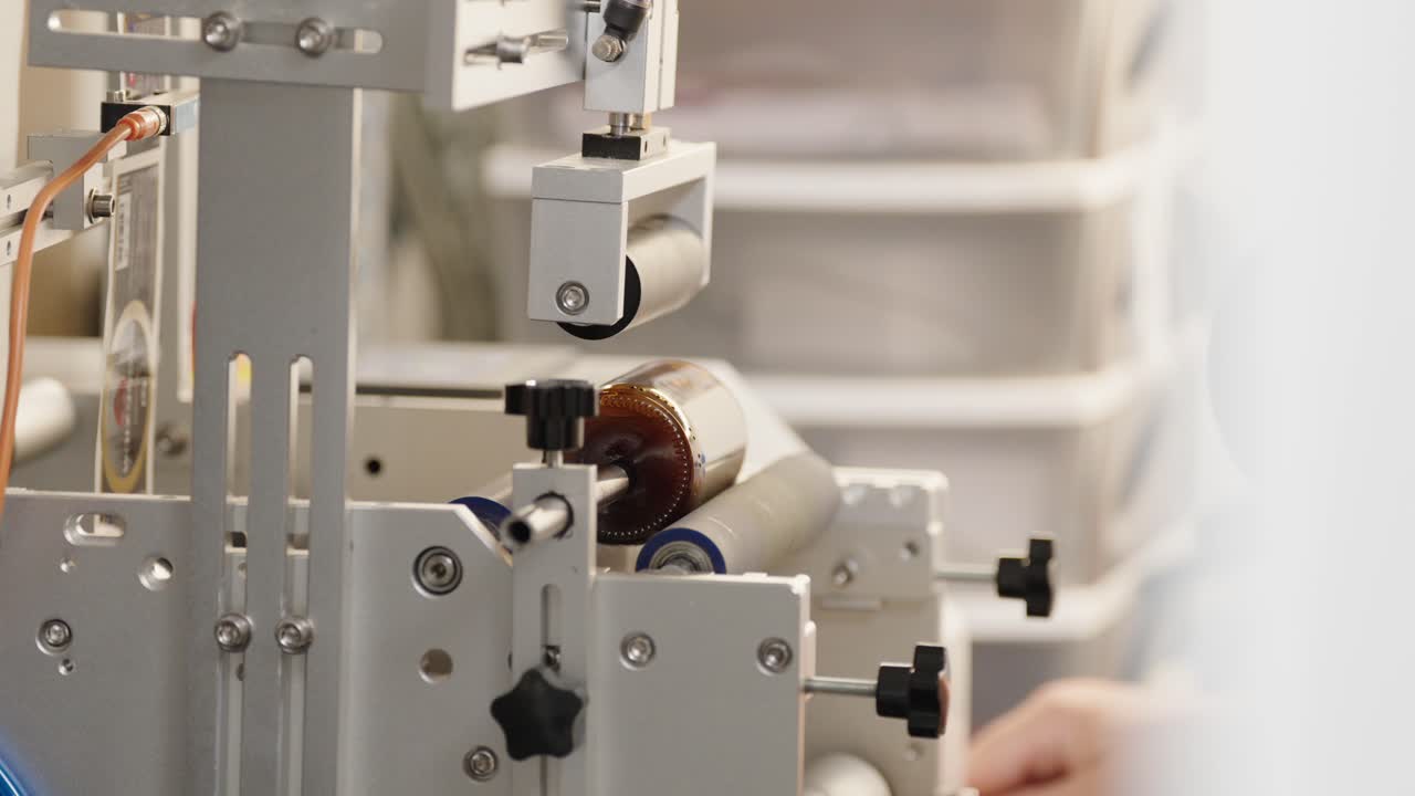 Close-up of an industrial labeling machine applying a label to a brown glass bottle in a pharmaceutical or cosmetic production facility