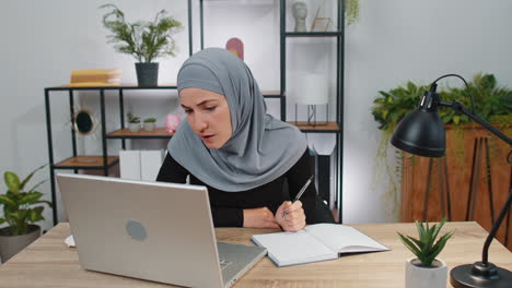 mujer de negocios musulmana estudiando con un cuaderno en la oficina de casa en una computadora portátil hablando con una cámara web en línea