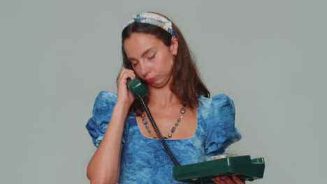 Crazy-girl-in-blue-dress-talking-on-wired-vintage-telephone-of-80s,-fooling-making-silly-faces