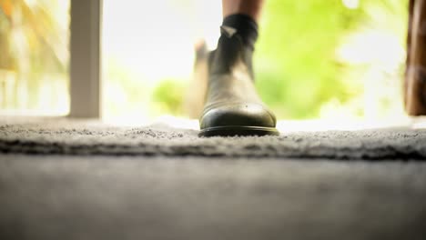 hombre entrando a la casa por la puerta abierta, quitándose las botas