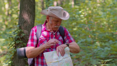 senior old tourist grandfather man lost and looking at map and compass while having walk in wood