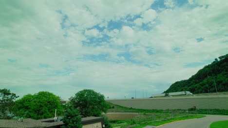 cloudy sky over a rest area with trucks passing by on the highway and green hills in the background.