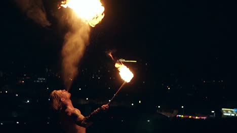 young blond male breathes out large stream of fire making fireball on black background slow motion