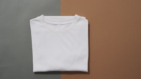 video of flat lay of folded white t shirt with copy space on grey and brown background