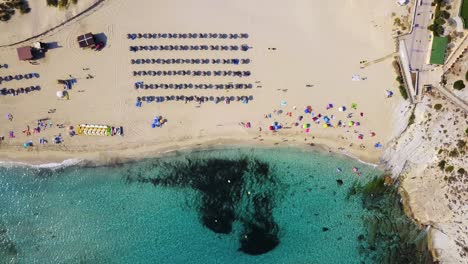 Playa-De-Cala-Mesquida-En-Mallorca-Con-Aguas-Turquesas-Y-Coloridas-Sombrillas,-Ambiente-Veraniego,-Vista-Aérea,-España,-En-El-Mar-Mediterráneo