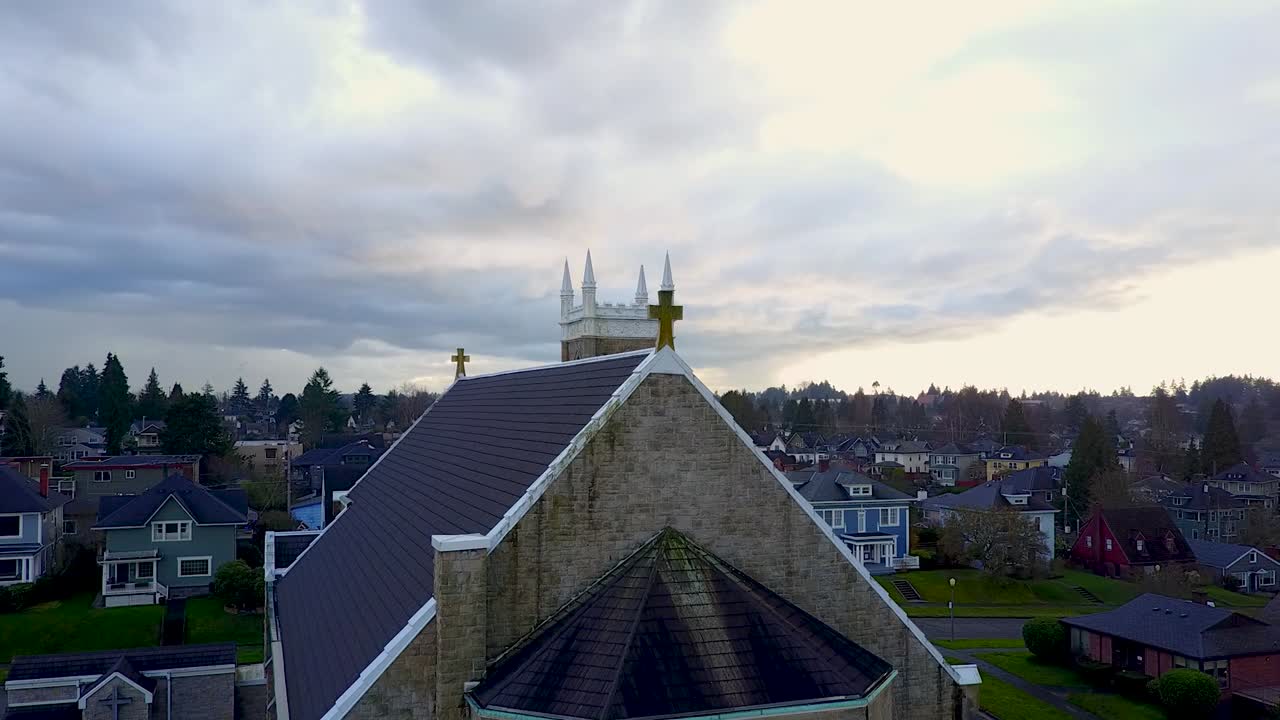 slowly rotating aerial shot of a cross on the roof of a church, stormy sky in the background