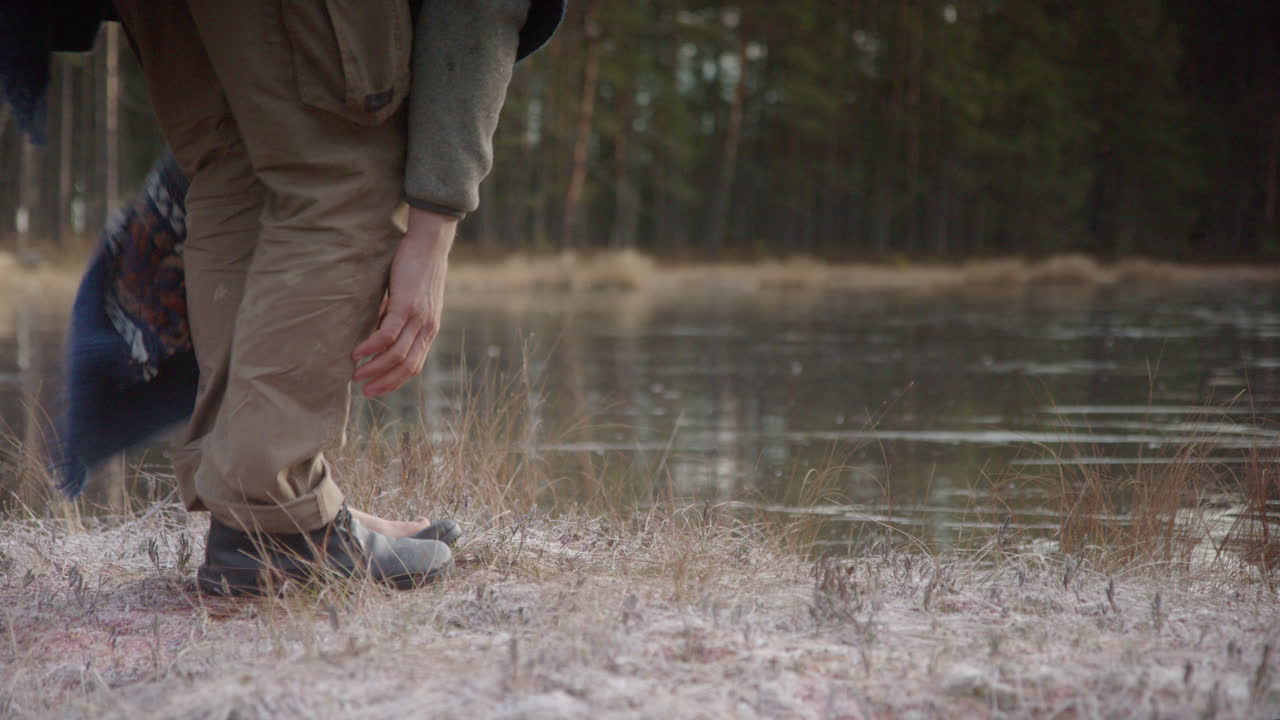TRACKING shot of an ice bather removing shoes and socks in front of frozen lake