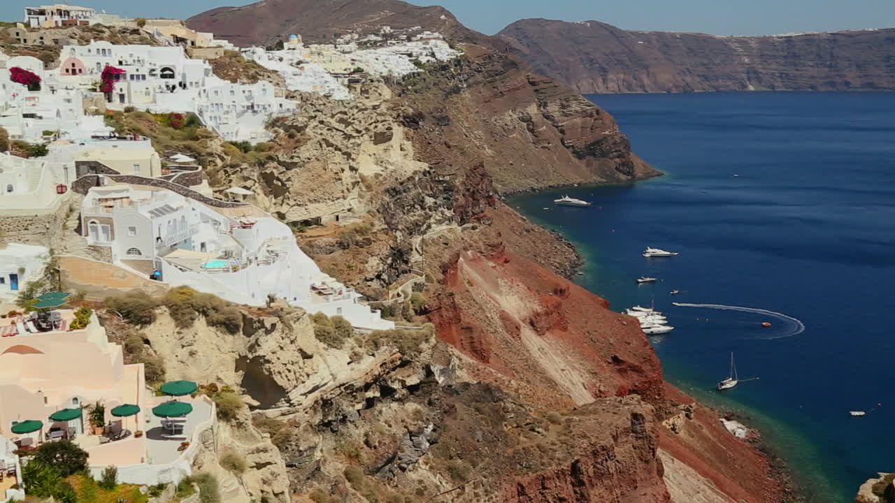 panorámica lenta de casas blancas que bordean las laderas de la isla griega de santorini con una bandera griega en la distancia 1