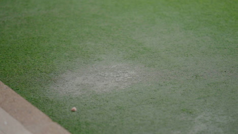 Rain-falling-on-a-synthetic-grass-carpet,-creating-a-wet-spot-and-showing-the-texture-of-the-artificial-turf