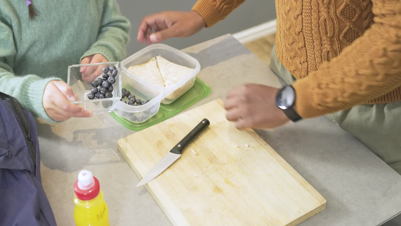 Padre e figlia afroamericani che tagliano un panino sul bancone, preparando il pranzo con mirtilli per la scuola.