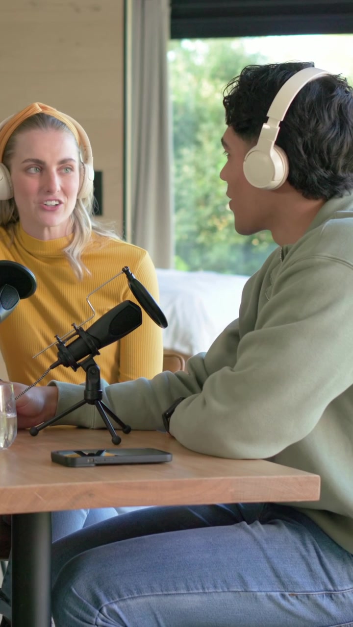 Video verticale: Uomo con felpa verde che si appoggia avviando un podcast, donna con maglietta gialla che parla a un microfono da tavolo