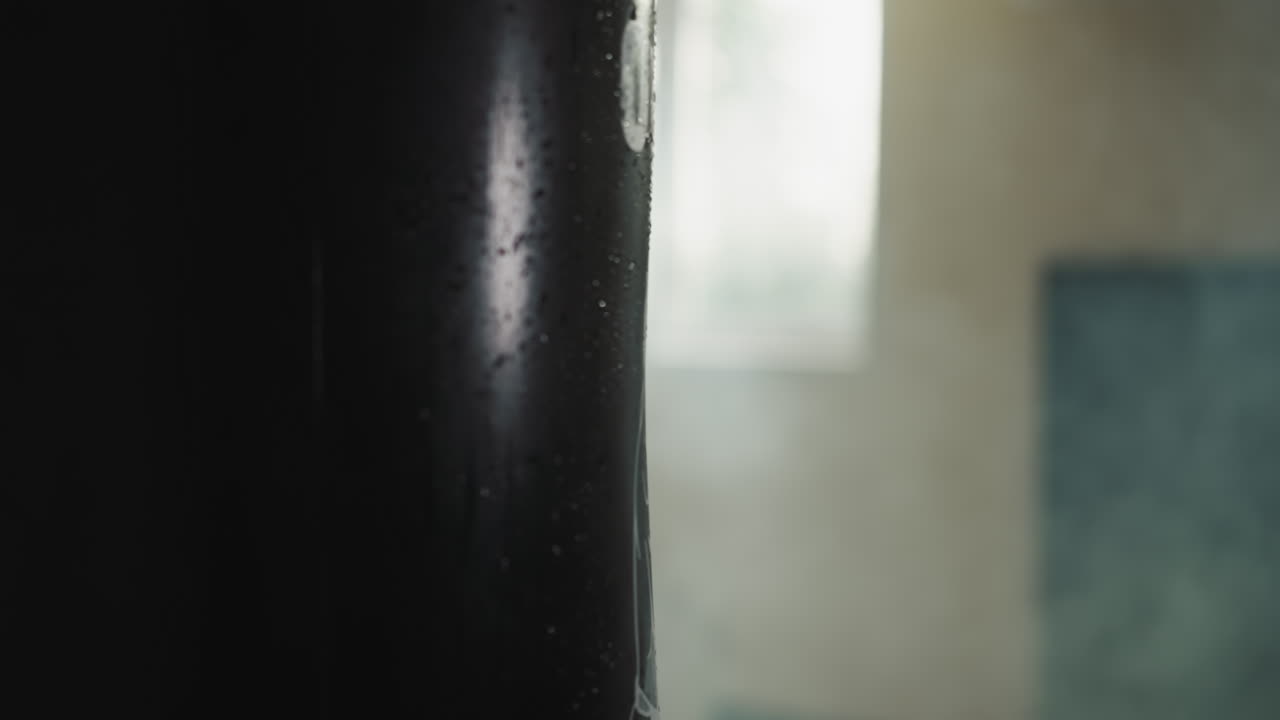 Strong athlete hand strikes punching bag with force using boxing glove in dark gym. Engaging in professional sports training in well equipped basement of sports club