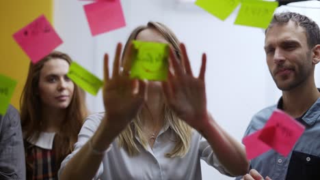 una mujer de negocios rubia en una reunión de equipo pega la nota de color en la pared de vidrio