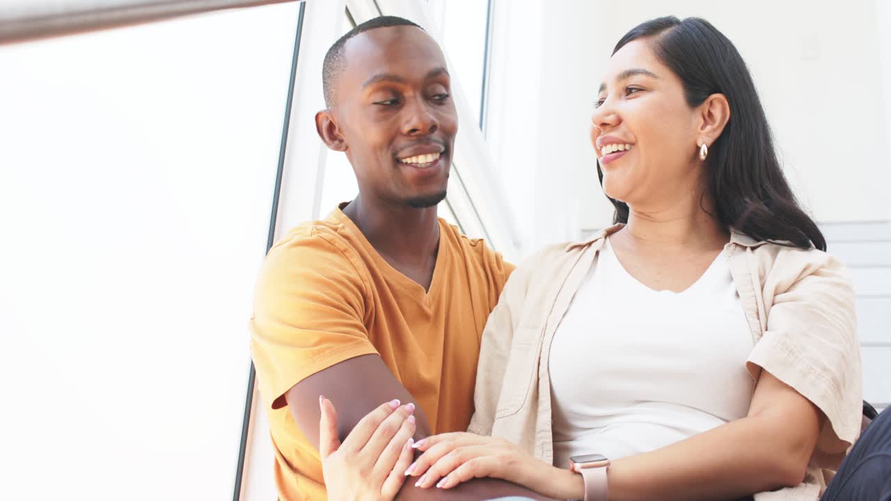 Laughing couple leaning on stair landing by window, man in mustard tee, woman in beige overshirt