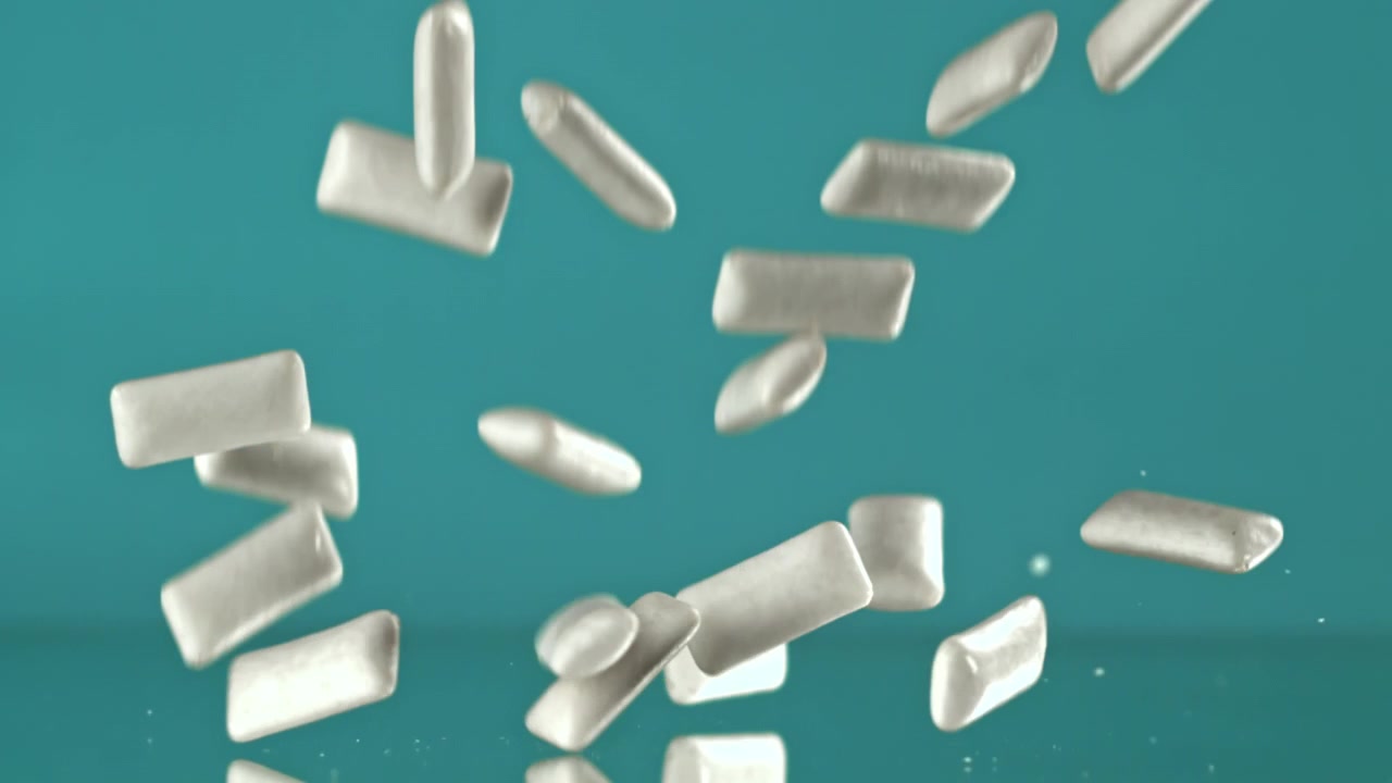 Pezzi di gomma da masticare bianchi che cadono e rimbalzano su una superficie riflettente verde acqua