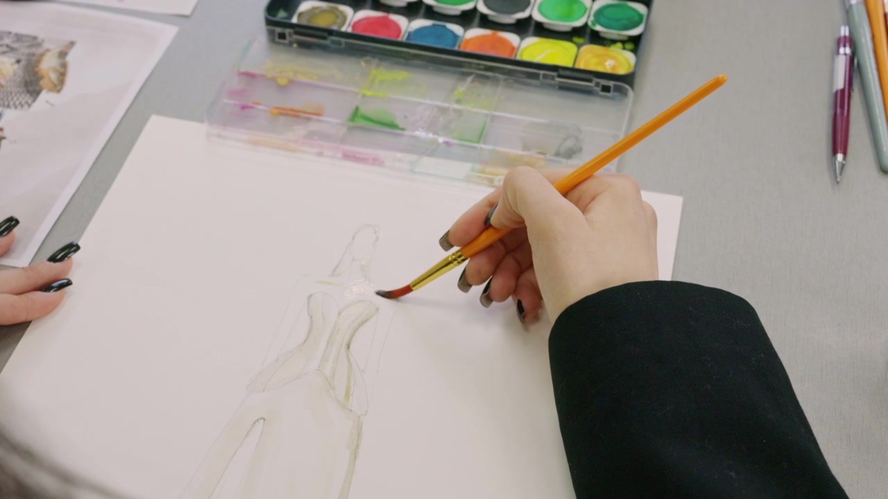 ภาพมุมสูงกว้างของนักเรียนแฟชั่นกำลังวาดภาพประกอบเสื้อผ้าบนโต๊ะออกแบบที่สะอาด