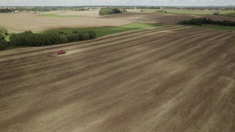 aerial shot big tractor on tracks pulling harrow system to recultivate soil of the big farm field - establishing shot