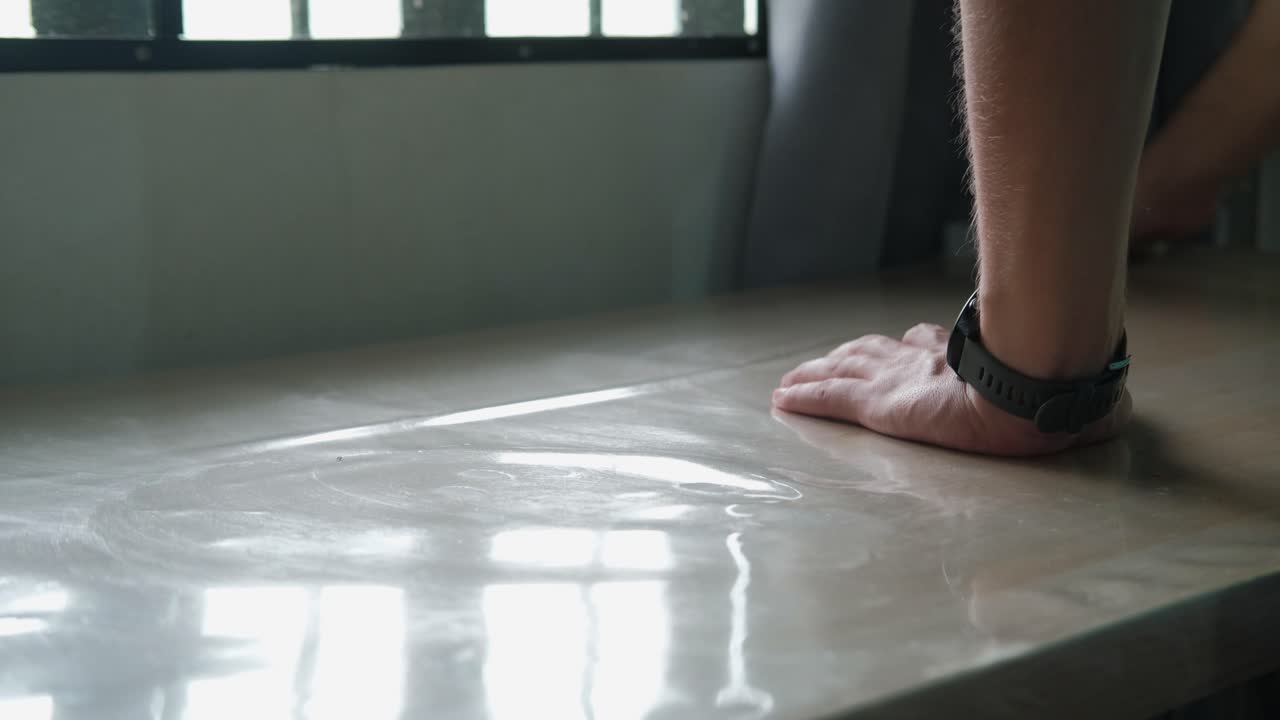 Close-up of male hands wiping down plastic-covered kitchen table surface.