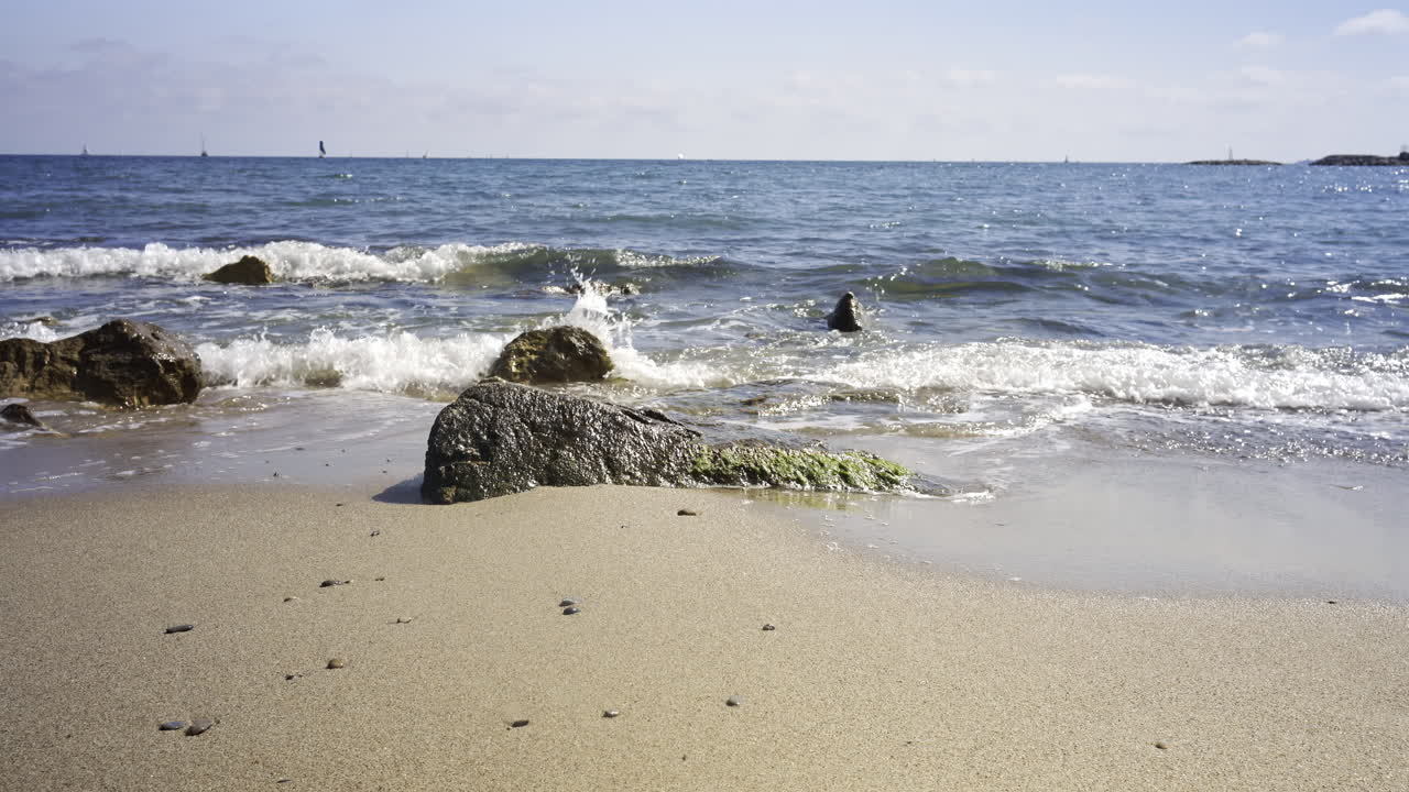 Waves crashing on rocks on a sandy beach in the south of France on a sunny day