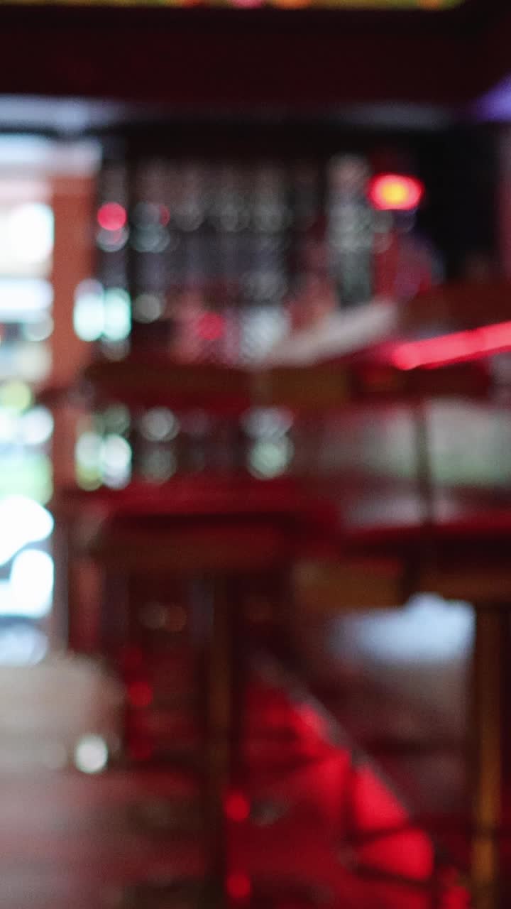 En person forlader en moderne bar eller restaurant med rød accentbelysning, mens kameraet forbliver stationært, og baggrunden gradvist kommer i fokus