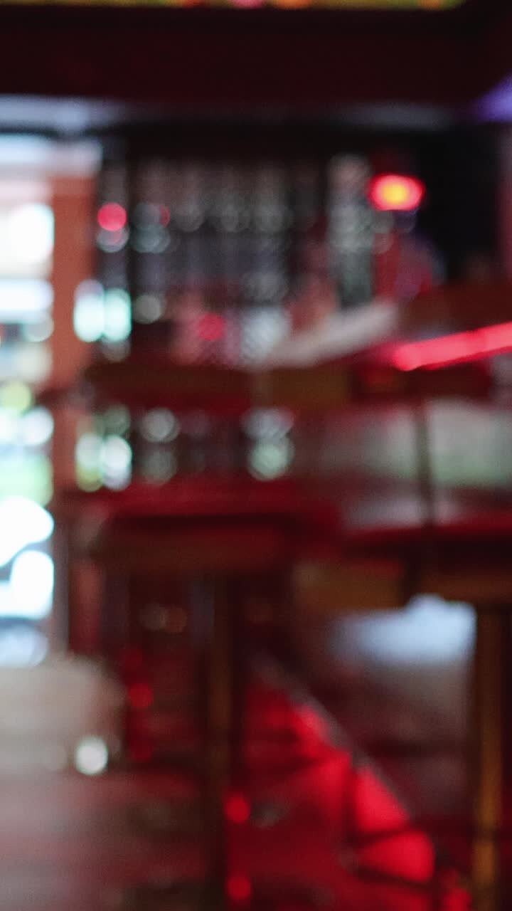 Una persona esce da un bar o ristorante moderno con illuminazione d'accento rossa, mentre la telecamera rimane ferma e lo sfondo si mette gradualmente a fuoco