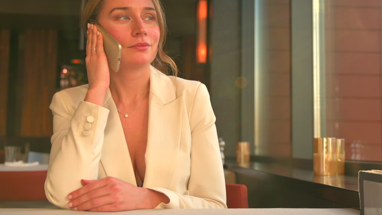 Donna con blazer bianco che parla al telefono in un ristorante