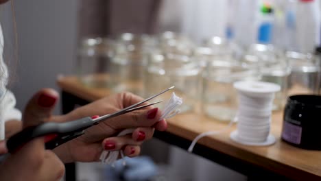 Young-woman-with-forearm-tattoos-and-red-nails-cutting-wicks-to-make-homemade-candles