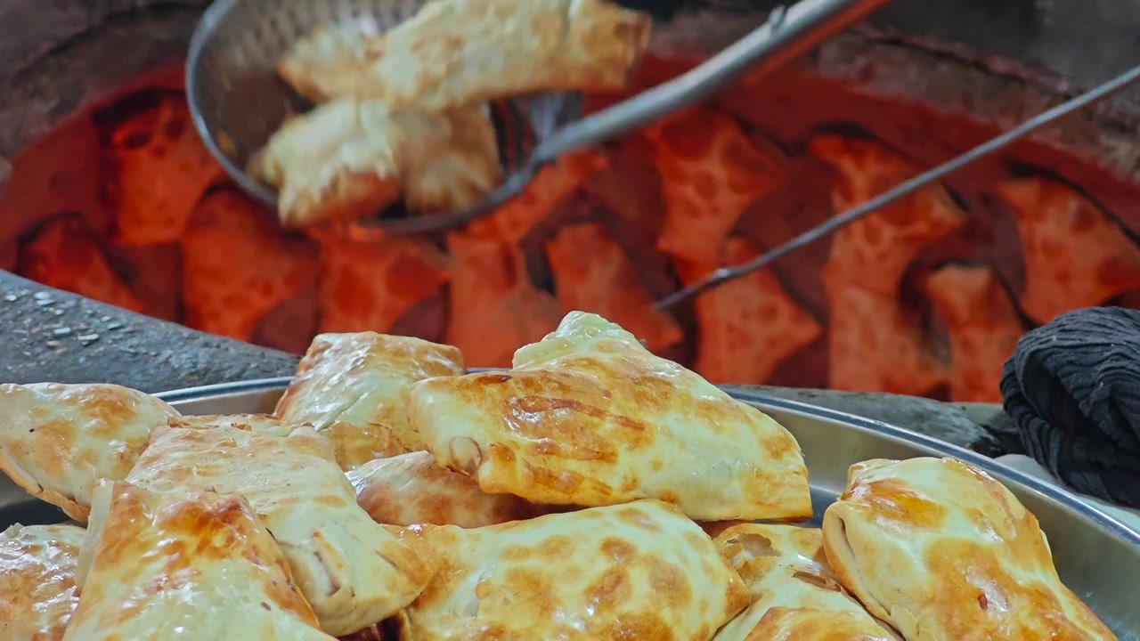Fornaio che rimuove samsa appena sfornati da un tradizionale forno tandoor