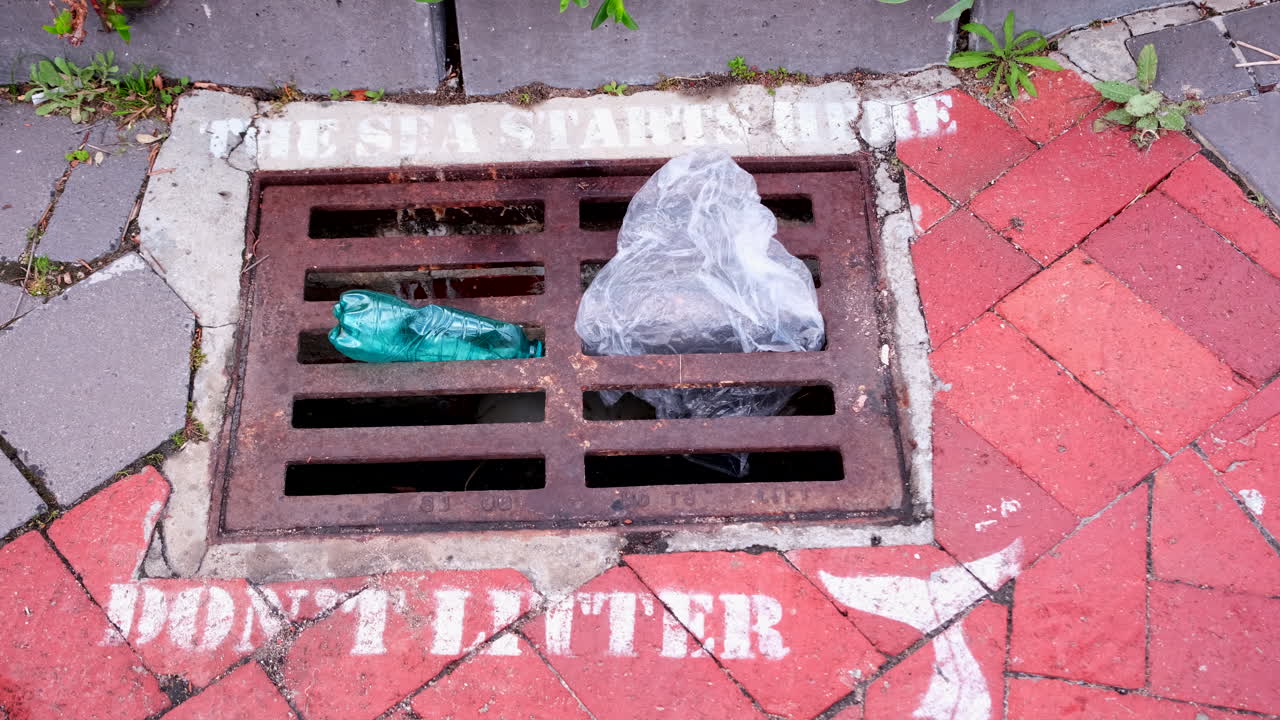 Ironic telephoto view of rainwater drain grate warning public not to litter with plastic bottle and bag stuck in it