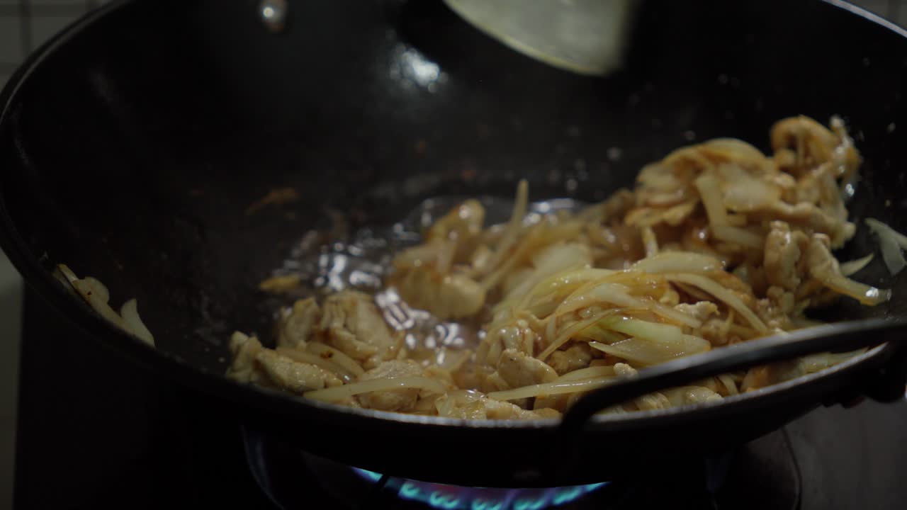 Versare acqua su cipolle bianche e carne di pollo saltate in un wok di metallo.