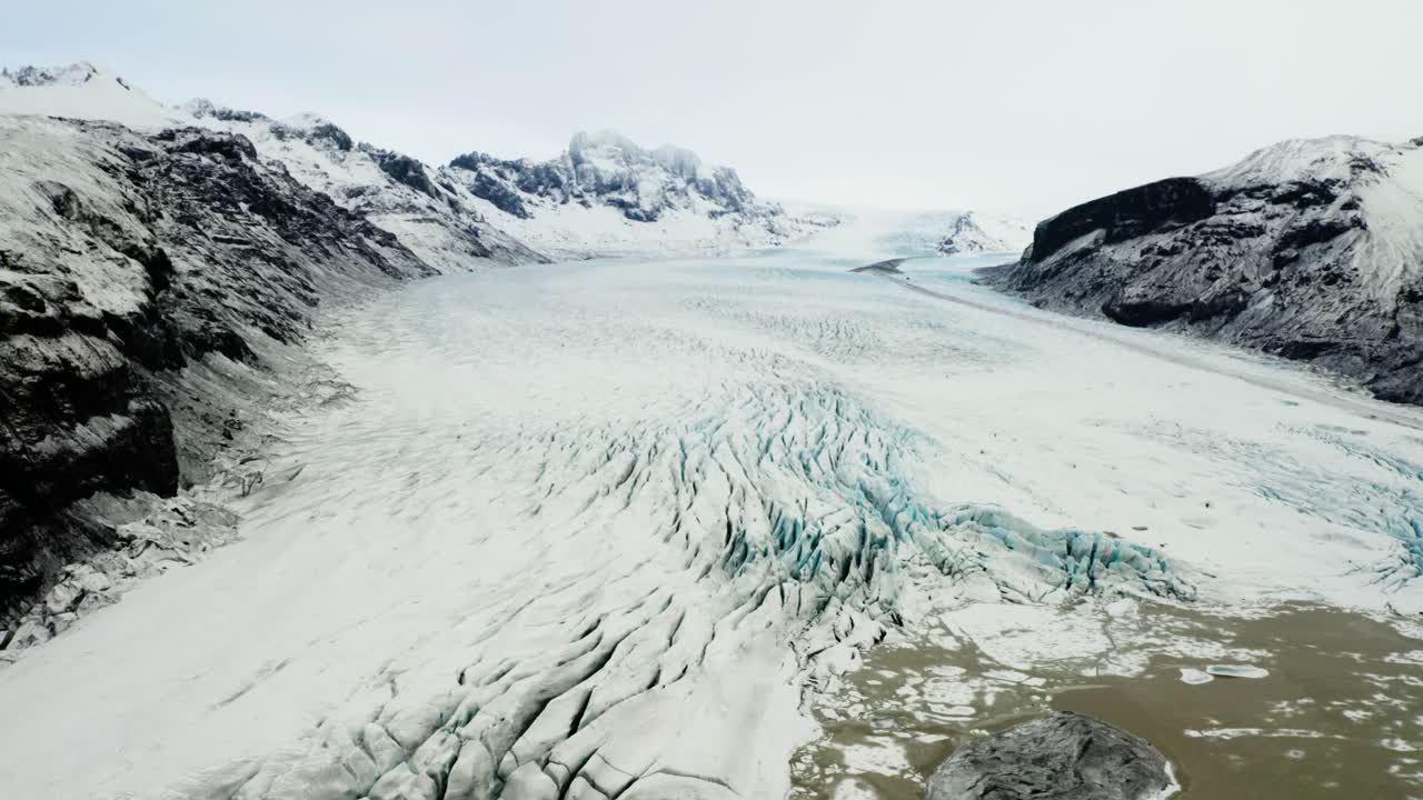 Stunning aerial footage capturing the intricate ice patterns, deep crevasses, and surrounding cliffs of this breathtaking glacier in Iceland.