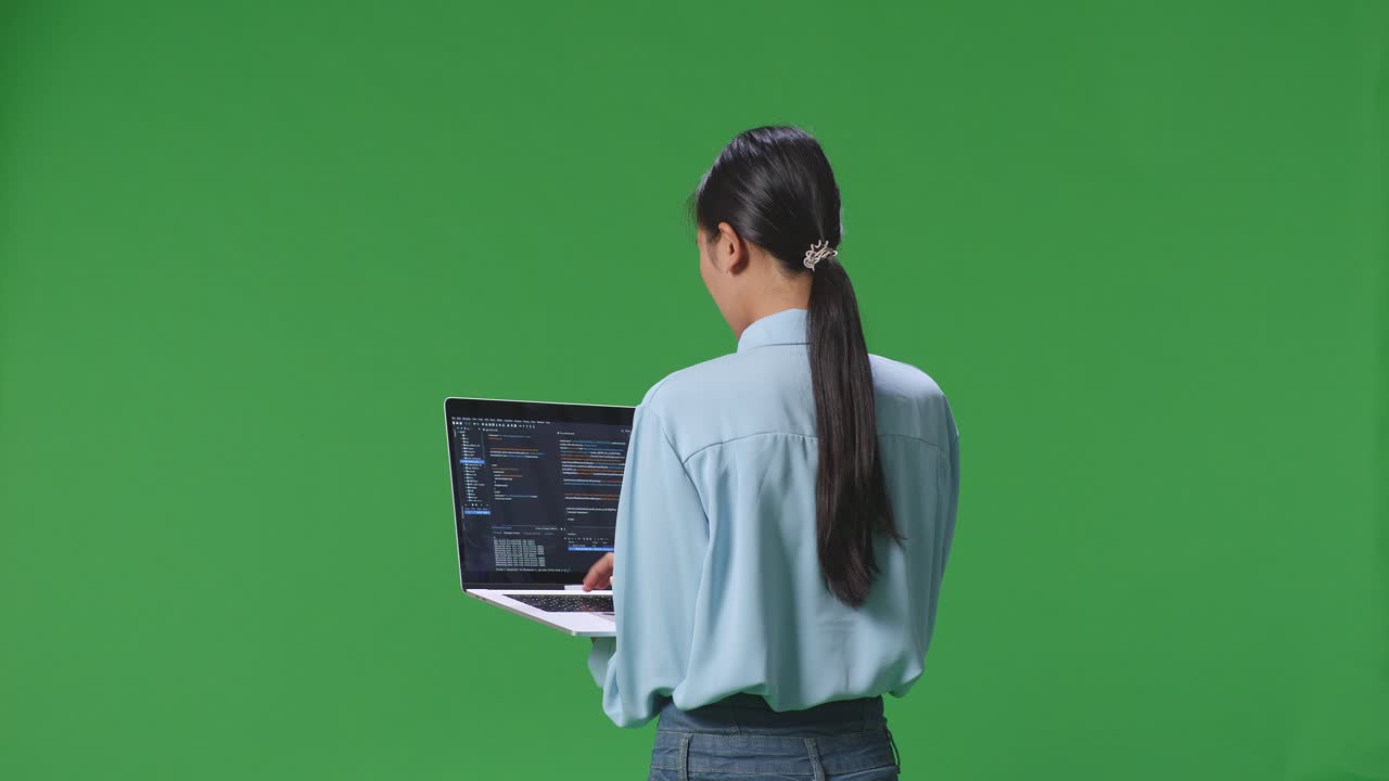 vista trasera de una mujer de negocios asiática usando una computadora portátil en un fondo de pantalla verde en el estudio, la pantalla de la computadora muestra el código