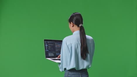 스튜디오에서 녹색 화면 배경에서 노트북 컴퓨터를 사용하는 아시아 사업가 여성의 뒷면, 컴퓨터 디스플레이가 코드를 보여줍니다.