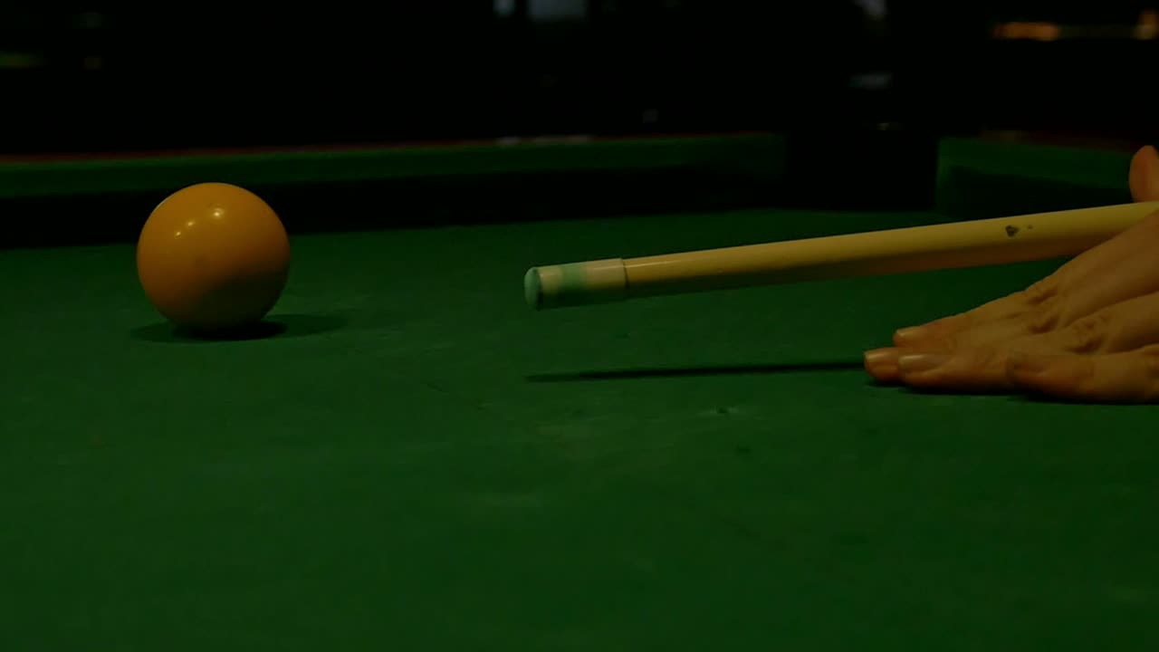 Primer plano, cámara lenta, taco de billar apoyado en la mano apunta y golpea una bola en la mesa de billar