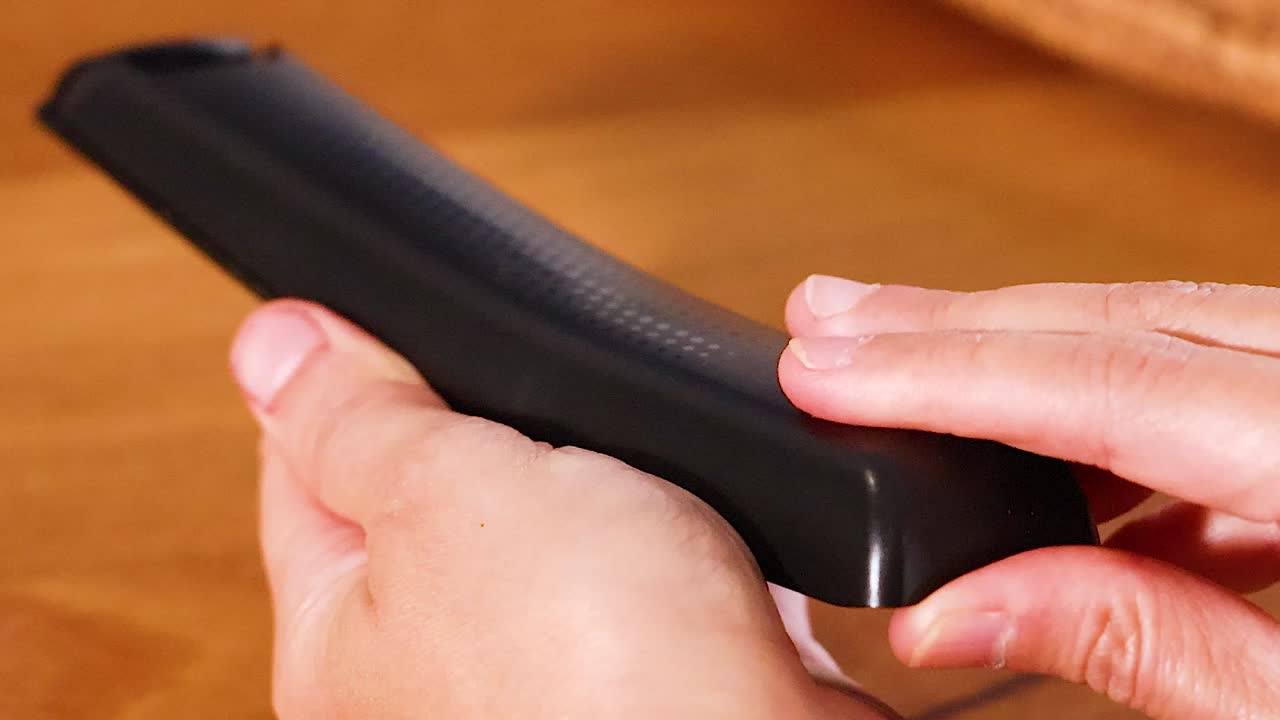 Primo piano dettagliato di mani che aprono scorrendo e rimuovono il coperchio posteriore di un telecomando.