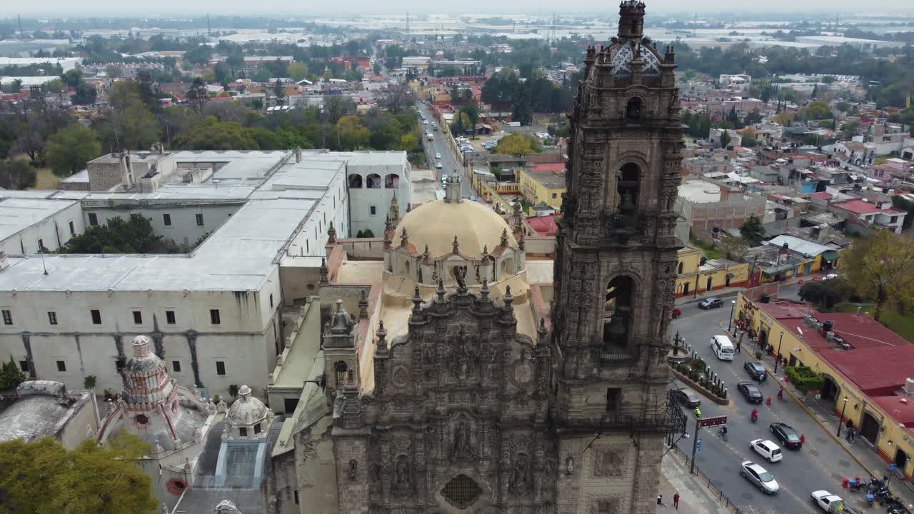 una toma de drone de una iglesia de la basílica de tepoztlan con algunas calles y coches pasando justo en un día nublado y soleado