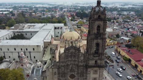 A-drone-shot-of-a-Tepoztlan-Basilica-church-with-some-streets-and-cars-passing-by-right-in-a-cloudy-sunny-day