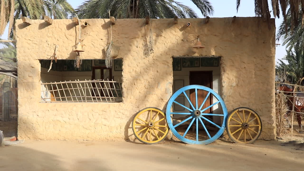 Ruote dipinte a colori vivaci contro un'antica casa di mattoni di fango a Sbeitla, di giorno