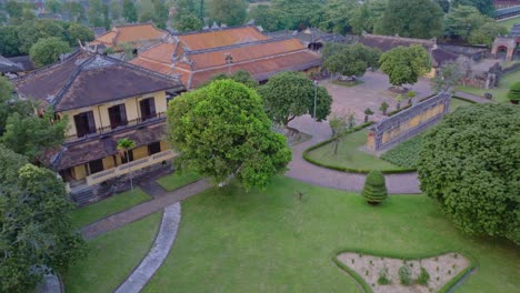 this footage captures an aerial view of the hue imperial city in vietnam, showcasing its impressive traditional architecture with yellow walls and red tiled roofs, surrounded by lush green trees.