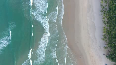 Aerial-of-ocean-waves-crashing-into-white-sand-beach-filmed-from-above-by-drone