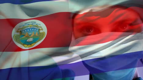 Animation-of-waving-costa-rica-flag-over-caucasian-female-surgeon-wearing-surgical-mask-at-hospital