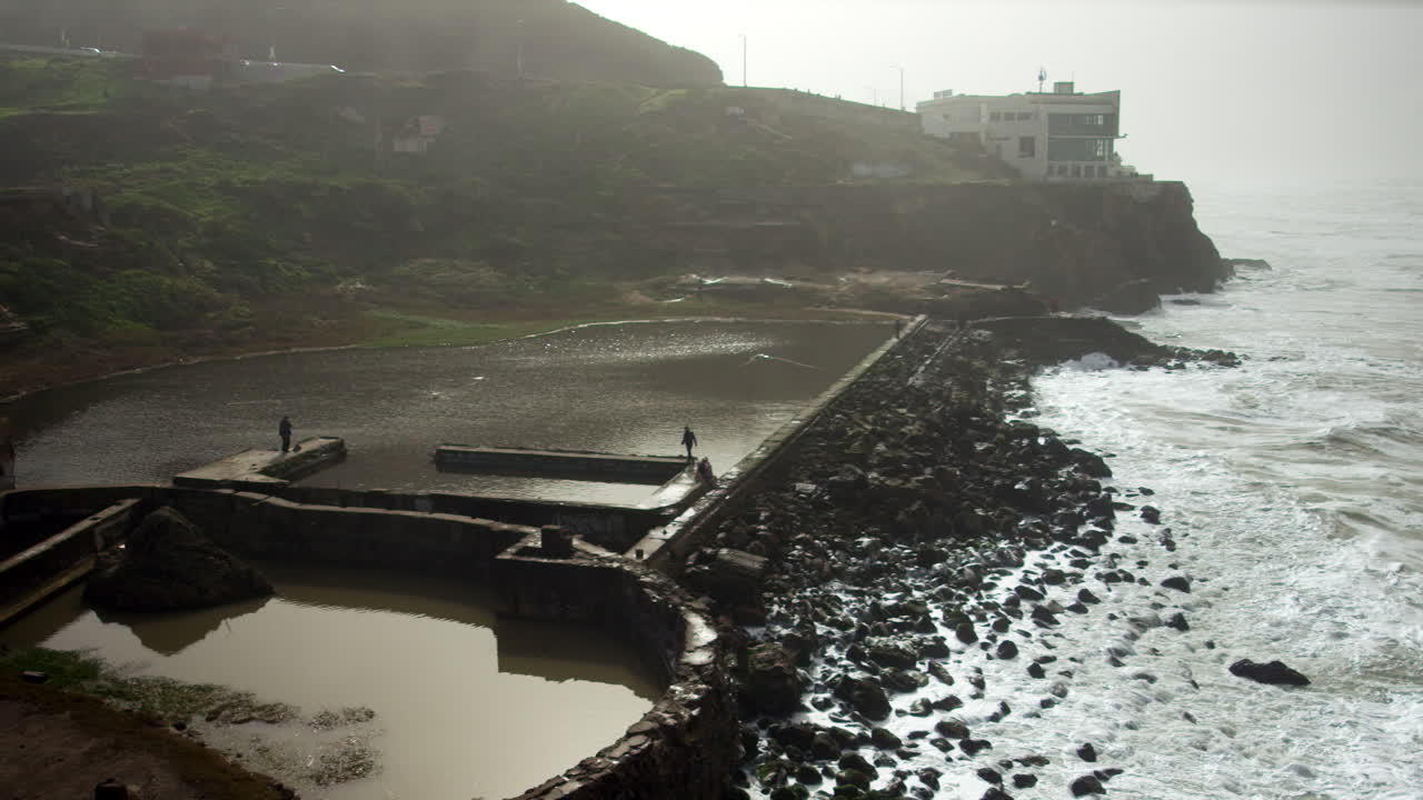 SLOW MOTION HD footage of waves rolling up to rocky beach below cliffside house