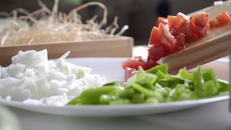 부엌에서 피망과 양파를 곁들인 접시에 토마토 조각을 넣는 사람